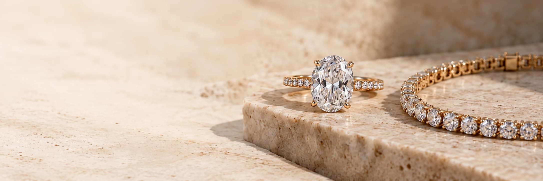 Oval diamond engagement ring and diamond tennis bracelet in yellow gold resting on warm travertine