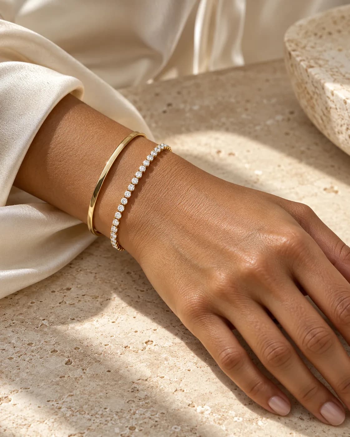 A diamond tennis bracelet and gold bangle worn on the wrist